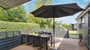 Eine Terrasses mit Tisch und Stühlen, einem großen Sonnenschirm und einem Holzboden.