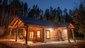 A log cabin with a porch, a covered outdoor seating area, and a well-lit interior. - Frontier Cabin, 7 min to Glacier, Fire Pit (Coram)