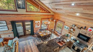 A spacious wooden cabin with a dining area, kitchen, and large windows overlooking a forest. - Frontier Cabin, 7 min to Glacier, Fire Pit (Coram)