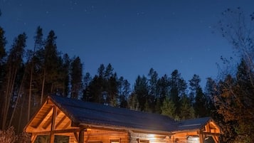 A wooden cabin with a porch, a covered outdoor seating area, and a well-lit entrance.