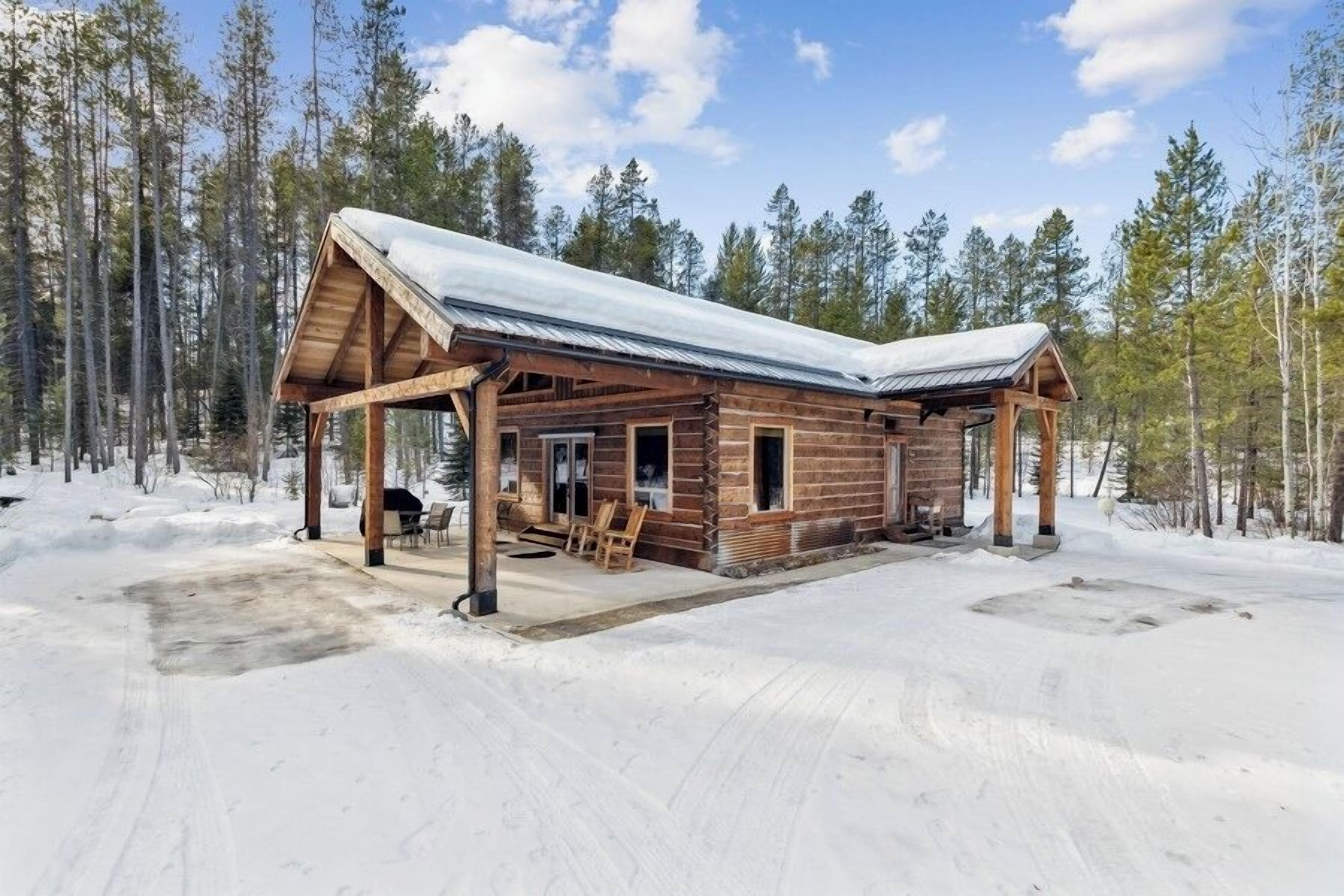 A wooden cabin with a metal roof, surrounded by a snowy landscape and tall trees.
