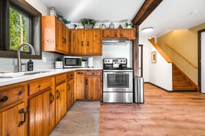 A modern kitchen with wooden cabinets, stainless steel appliances, and a view of the outdoors. - Saddle n` Sage, 7 min to Glacier, Fire Pit (Coram)