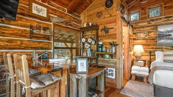 Ein Interieur einer Holzhütte mit einem Essbereich aus Holz, einer Küche mit an der Wand hängenden Kochutensilien und einem Bett mit Blick.