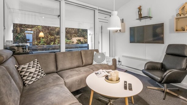 Una sala de estar moderna con un sofá, una mesa redonda de centro, un sillón de cuero negro y un televisor montado en la pared.