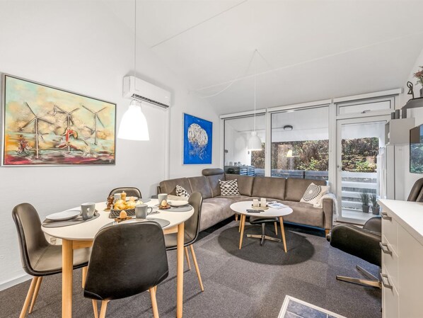 A modern living room with a dining area, a sofa, and a coffee table. There is a painting on the wall, a window with a view, and a ceiling fan. - "Soffhie" - 250m from the sea by Interhome (Ringkøbing)