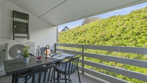 Un balcón con una mesa, sillas, un ventilador y vistas a una ladera verde.