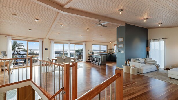 A spacious living area with a high ceiling, wooden flooring, a dining area, and a view of the outdoors.