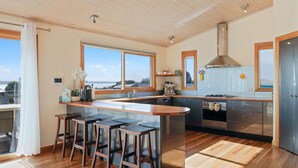 A modern kitchen with a central island, bar stools, a large window, and a view of the sea.