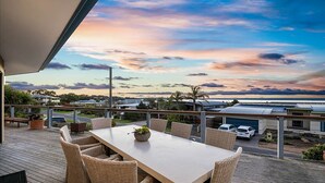 A terrace with a table and chairs, overlooking a residential area and a body of water during sunset.