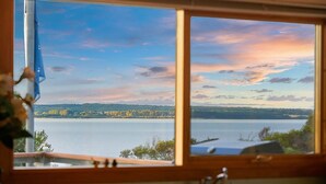 A view through a window of a lake with a distant shoreline, a clear sky, and a wooden window frame.