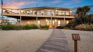 A modern beachfront property with a covered outdoor area, a wooden deck, and a number sign indicating the property number.