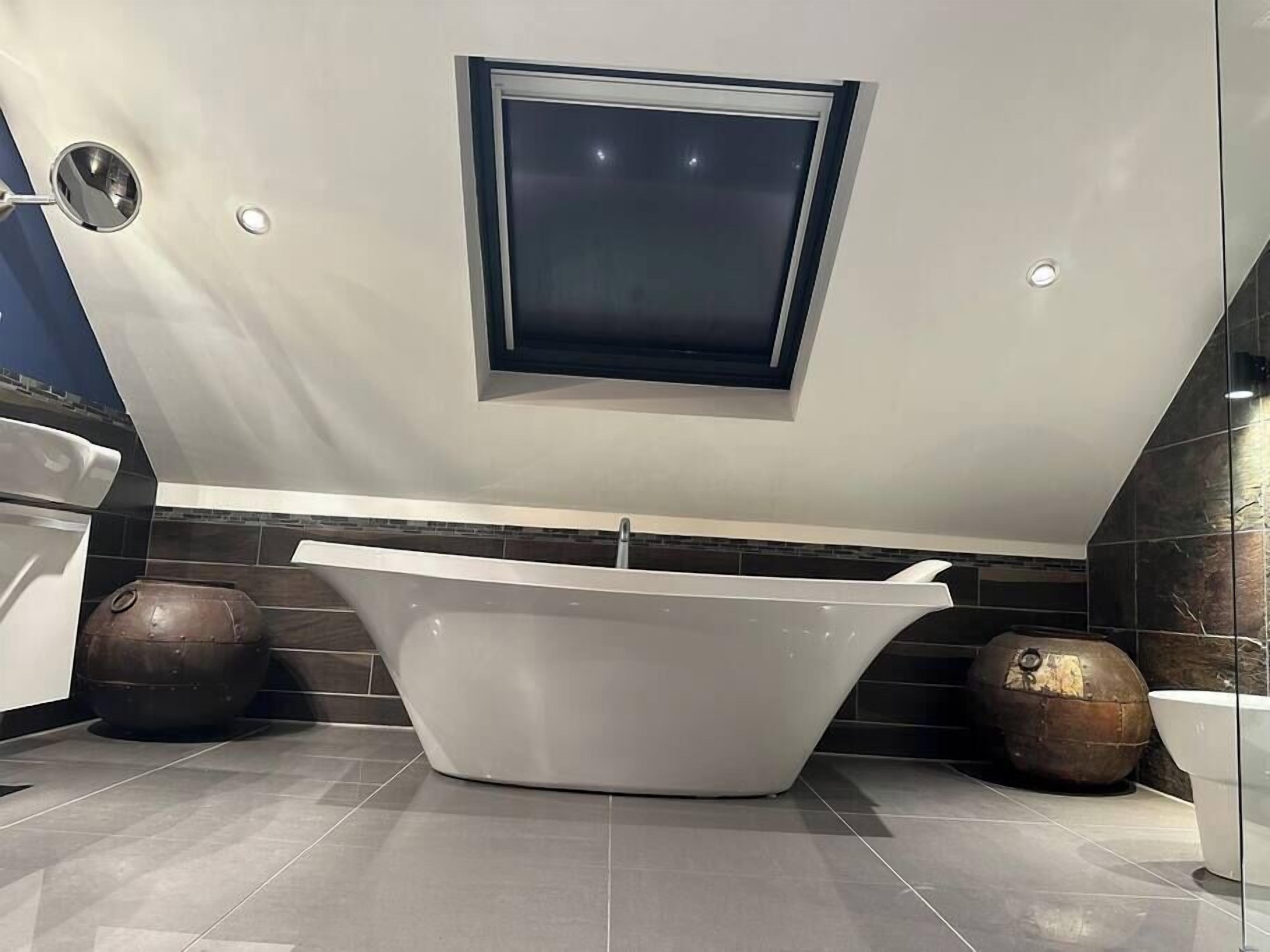 Un baño moderno con una bañera independiente, un pequeño ventanal sobre la bañera y jarrones decorativos en el suelo.