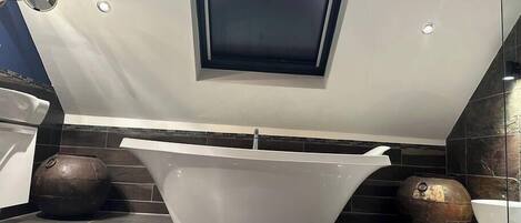 Un baño moderno con una bañera independiente, un pequeño ventanal sobre la bañera y jarrones decorativos en el suelo.