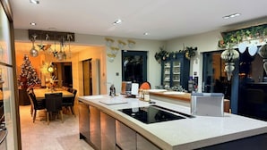 A modern kitchen with a central island, built-in appliances, and a dining area with a Christmas tree. - Riverside Country Retreat, Holiday Rental HotTub  Pizza Oven (Kirtlebridge)
