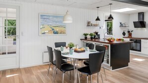 A modern kitchen with white cabinetry, a dining area with a white table and black chairs, and a large window with a view of greenery. - "Eli" - 1.5km to the fjord by Interhome (Blåvand)