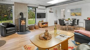 A modern living room with a fireplace, a dining area, and a large window offering a view of the outdoors. - "Eli" - 1.5km to the fjord by Interhome (Blåvand)