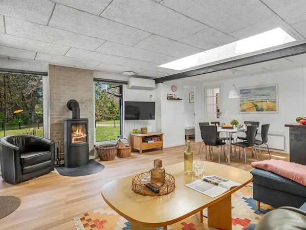 A modern living room with a fireplace, a dining area, and a large window offering a view of the outdoors.