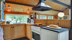 A kitchen with wooden cabinets, a stove, and a countertop with a bread display. - "Herlek" - 200m from the sea by Interhome (Knebel)