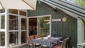 An outdoor dining area with a table and chairs, a large umbrella, and a wooden building with a sign above the door. - "Herlek" - 200m from the sea by Interhome (Knebel)