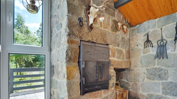 A stone fireplace with a modern wood-burning stove, stone walls, and a rustic decor including antlers and a basket of firewood. - "Herlek" - 200m from the sea by Interhome (Knebel)
