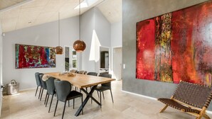 Un vaste espace dédié à la salle à manger, avec une longue table en bois, des chaises modernes et des luminaires suspendus.