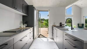 Une cuisine moderne dotée d’un îlot central, d’appareils électroménagers intégrés et donnant sur une terrasse extérieure.