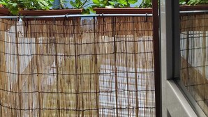 Une vue d’un bâtiment de style japonais traditionnel, avec un toit recouvert de tuiles, une fenêtre à cadre blanc et une clôture en bambou au premier plan.