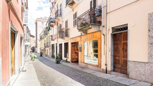 Une ruelle étroite pavée, bordée d’immeubles à plusieurs étages, dont certains sont dotés de balcons et de devantures de magasins.