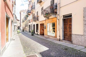 A narrow cobblestone street lined with multi-story buildings, some with balconies and storefronts. - Historical Center: Ca' Balenga, comfort & design (Asti)