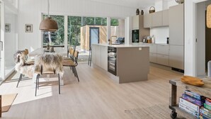 Une cuisine moderne dotée d’un îlot central, de planchers en bois et de grandes fenêtres offrant une vue sur l’extérieur.