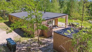Une cabane moderne dotée d’une terrasse, entourée d’arbres et d’une cour clôturée.