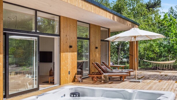 Un espace moderne aménagé à l’extérieur avec un bain à remous, une terrasse en bois, des chaises longues et un grand parasol.