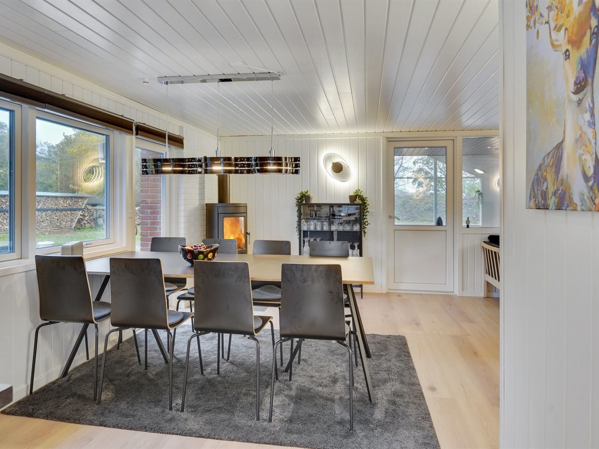Een moderne eetruimte met een houten tafel en stoelen, een open haard en een groot raam.