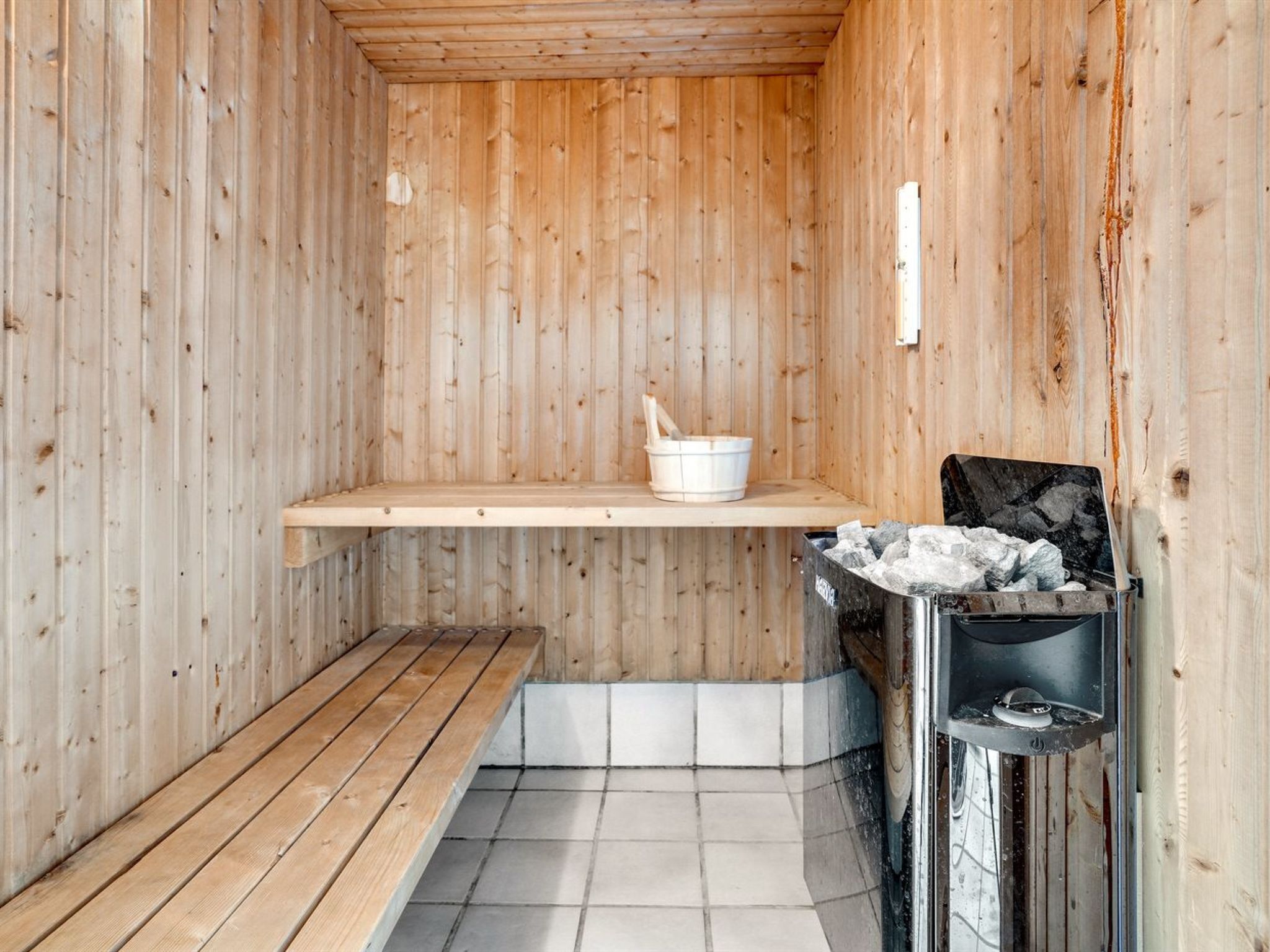 Een sauna met houten wanden, een bank, een plank met een emmer, en een sauna kachel.