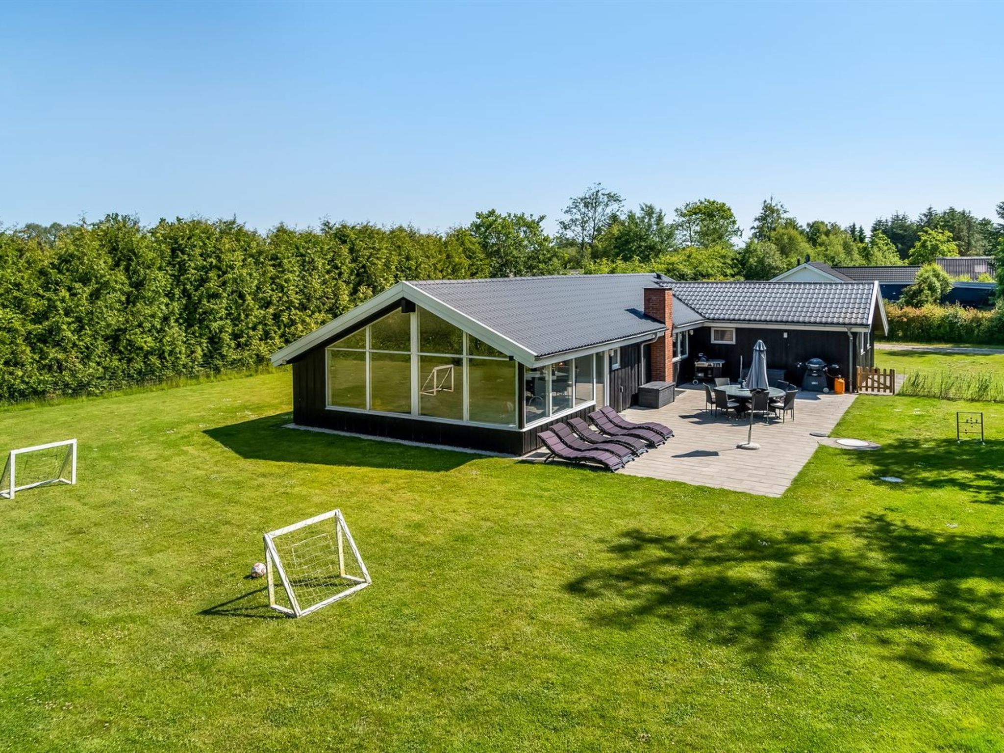Et moderne hus med et stort glasrum, en terrasse med udendørs møbler og en garage.