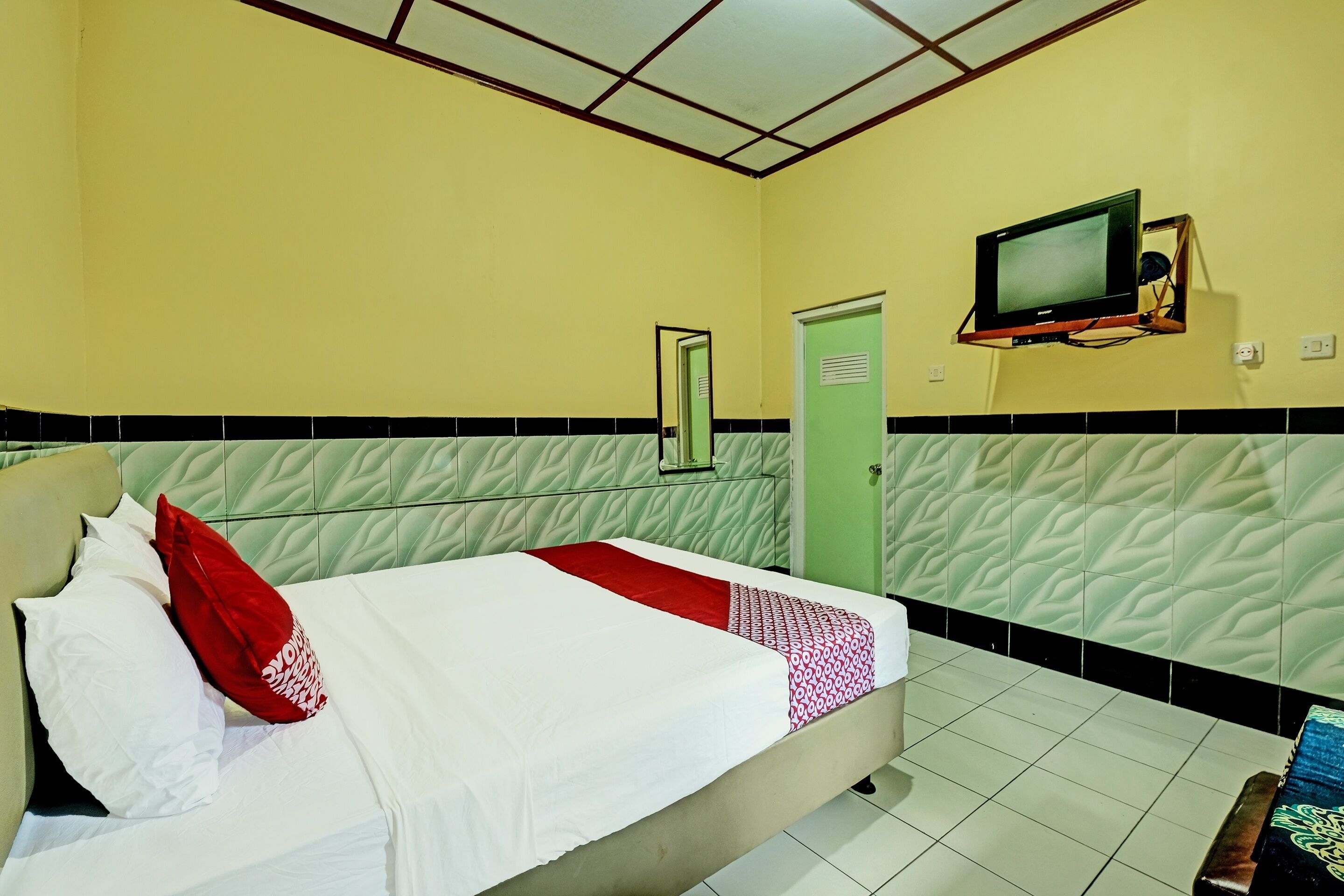 A hotel room with a bed, a television mounted on the wall, and a door.