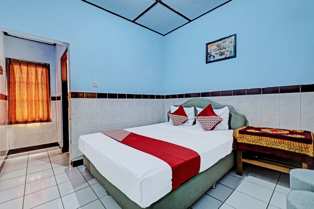 A hotel room with a bed, a bedside table, a chair, a window with curtains, and a wall-mounted picture.