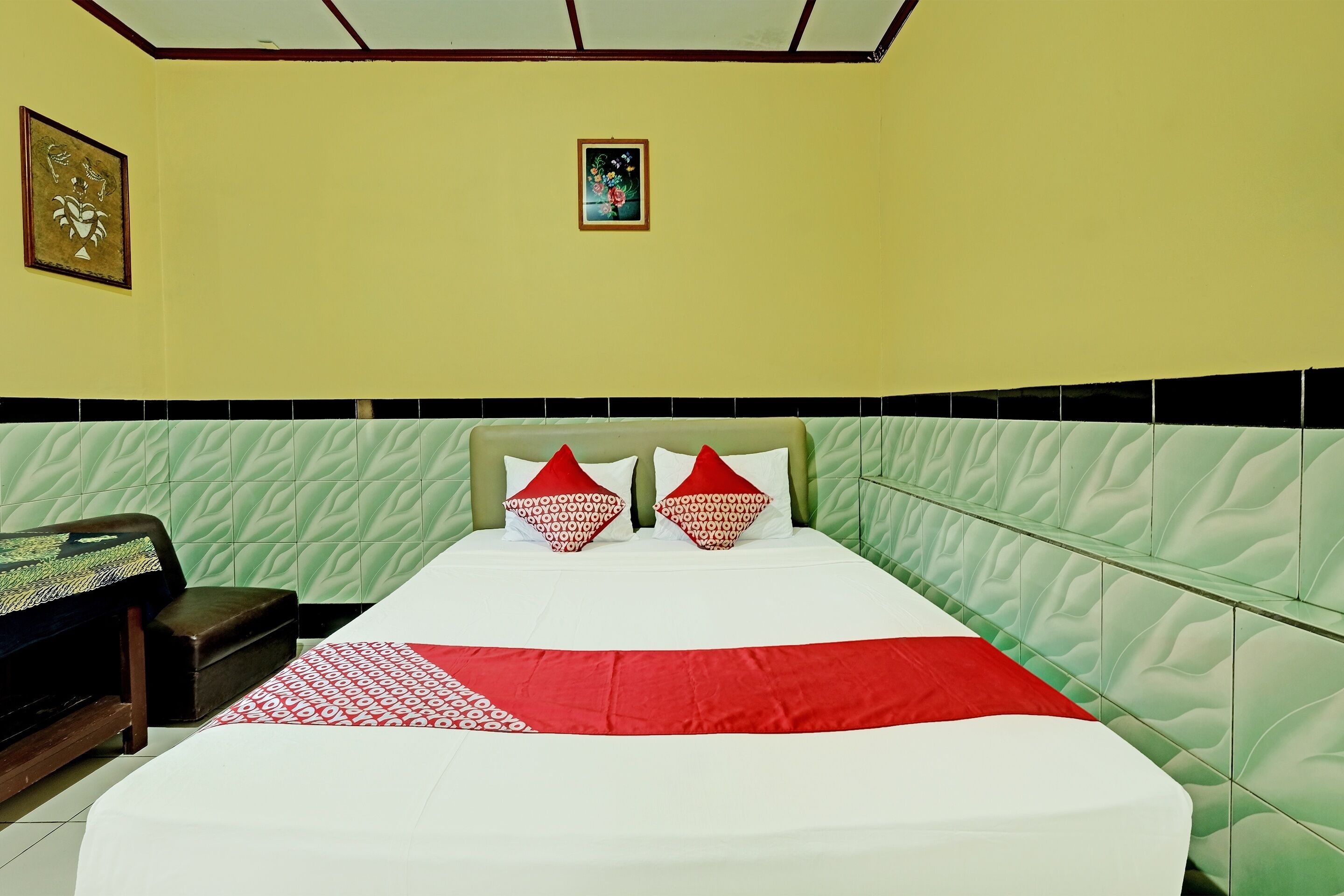Un lit bien fait, recouvert d’une couvre-lit à motifs rouges et blancs, agrémenté de deux coussins en forme de cœur et doté d’une tête de lit verte matelassée.