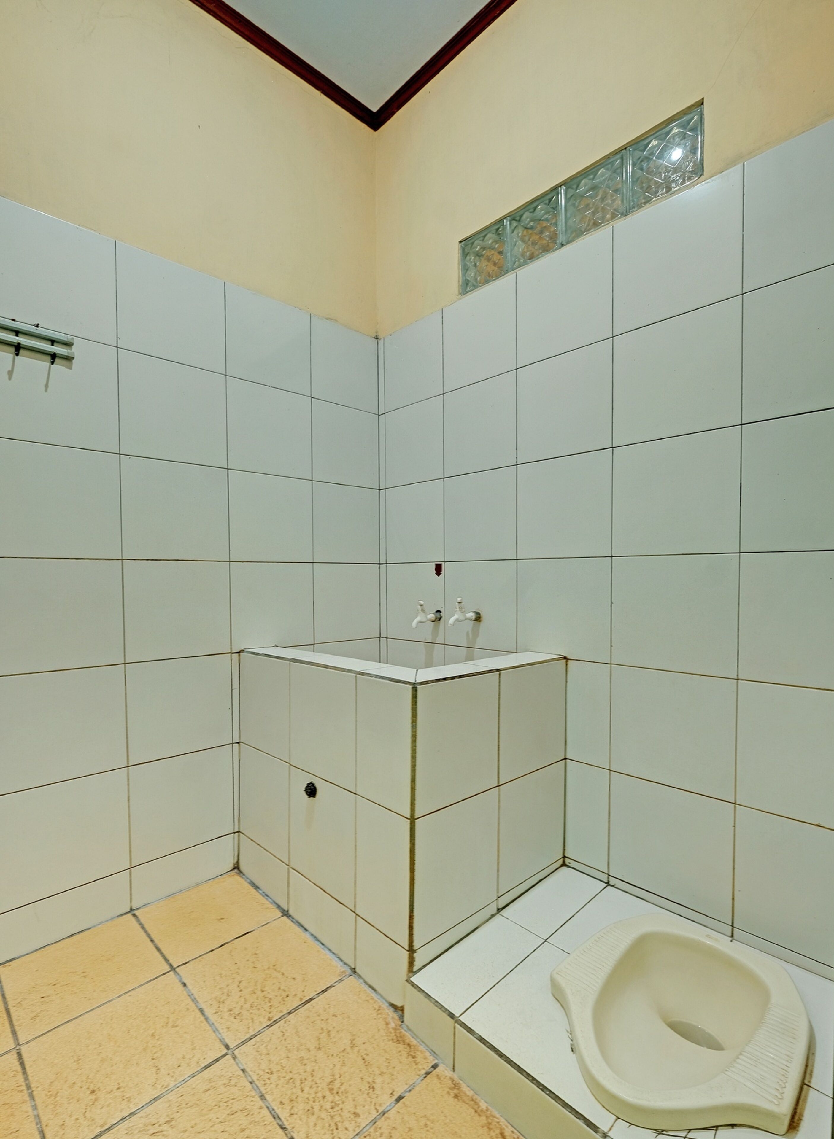 Et lille badeværelse med hvide fliser, et toilet og en vask med armatur.
