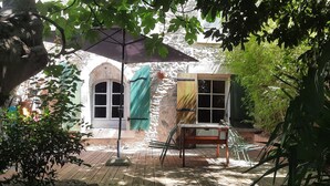 Un espacio al aire libre rústico con una mesa y sillas de madera, un paraguas de metal y un muro de piedra.