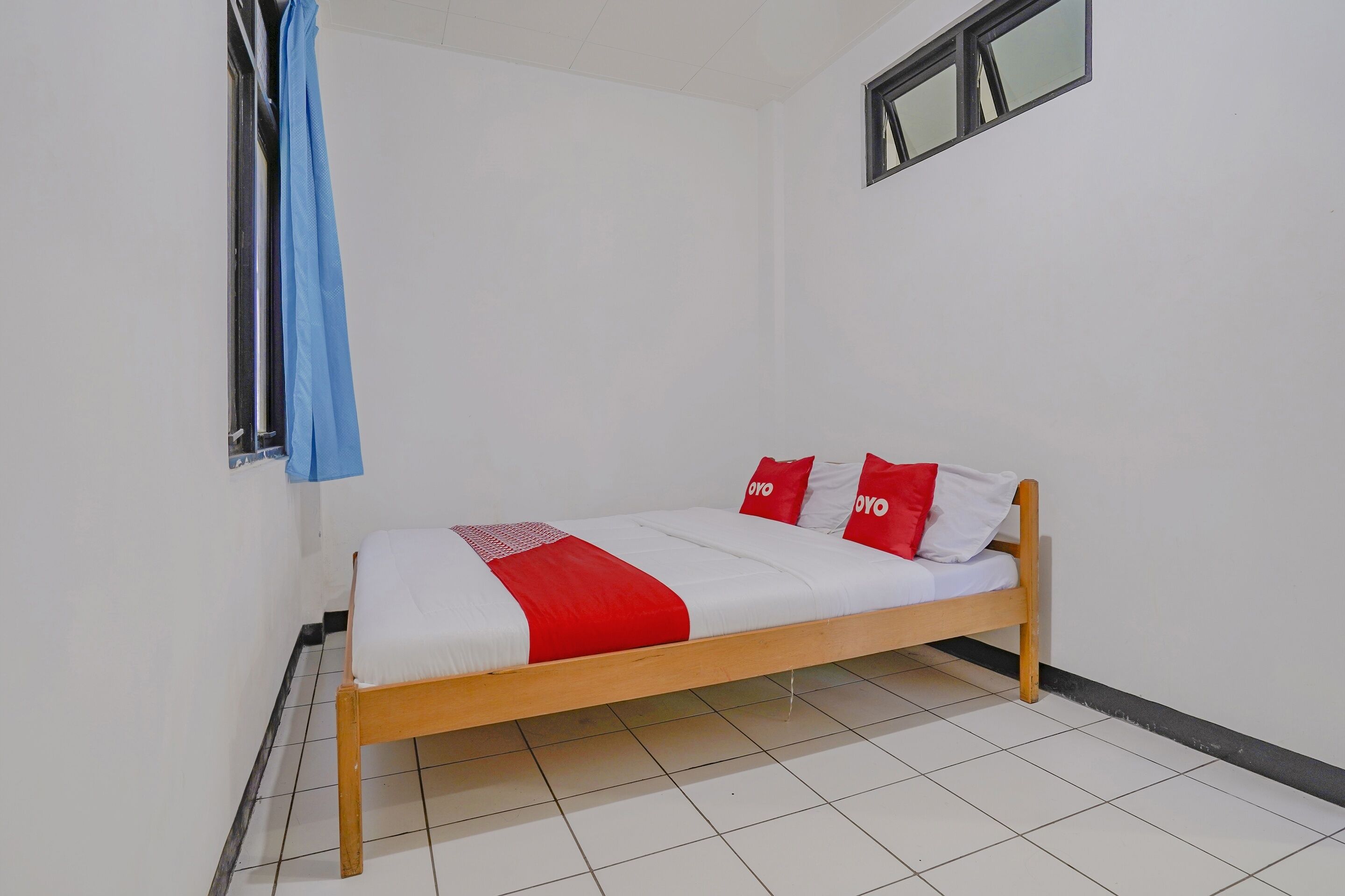 A single bed with a wooden frame, white bedding, and red accents.