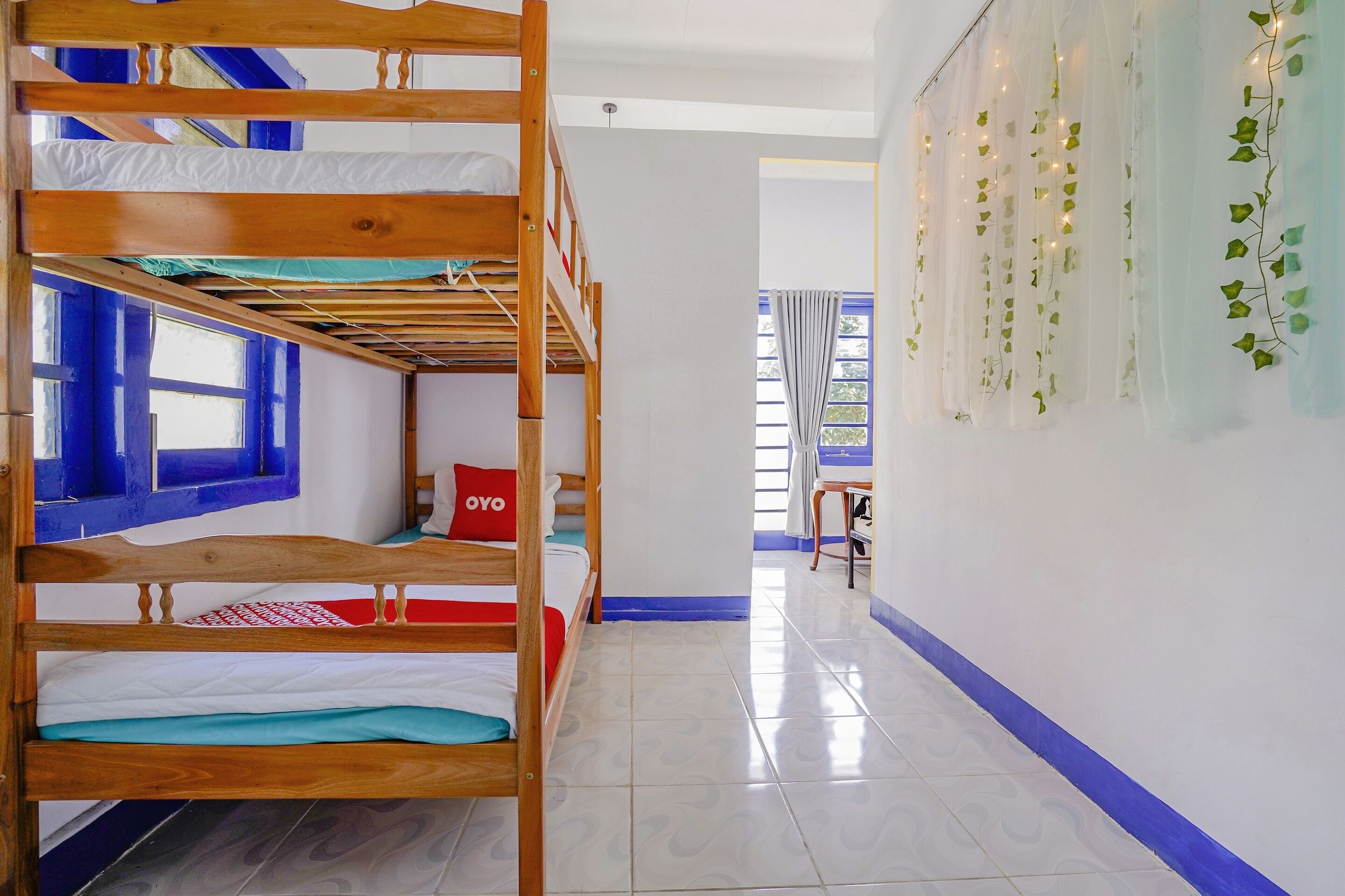 A bunk bed room with a window, a bed with a pillow labeled "OYO", and a wall with string lights and ivy.
