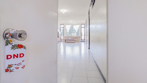 A hallway with a door labeled "DND" and a view of a living area with a sofa and a window. - OYO 90352 Villa Agape 2 (Cipanas)