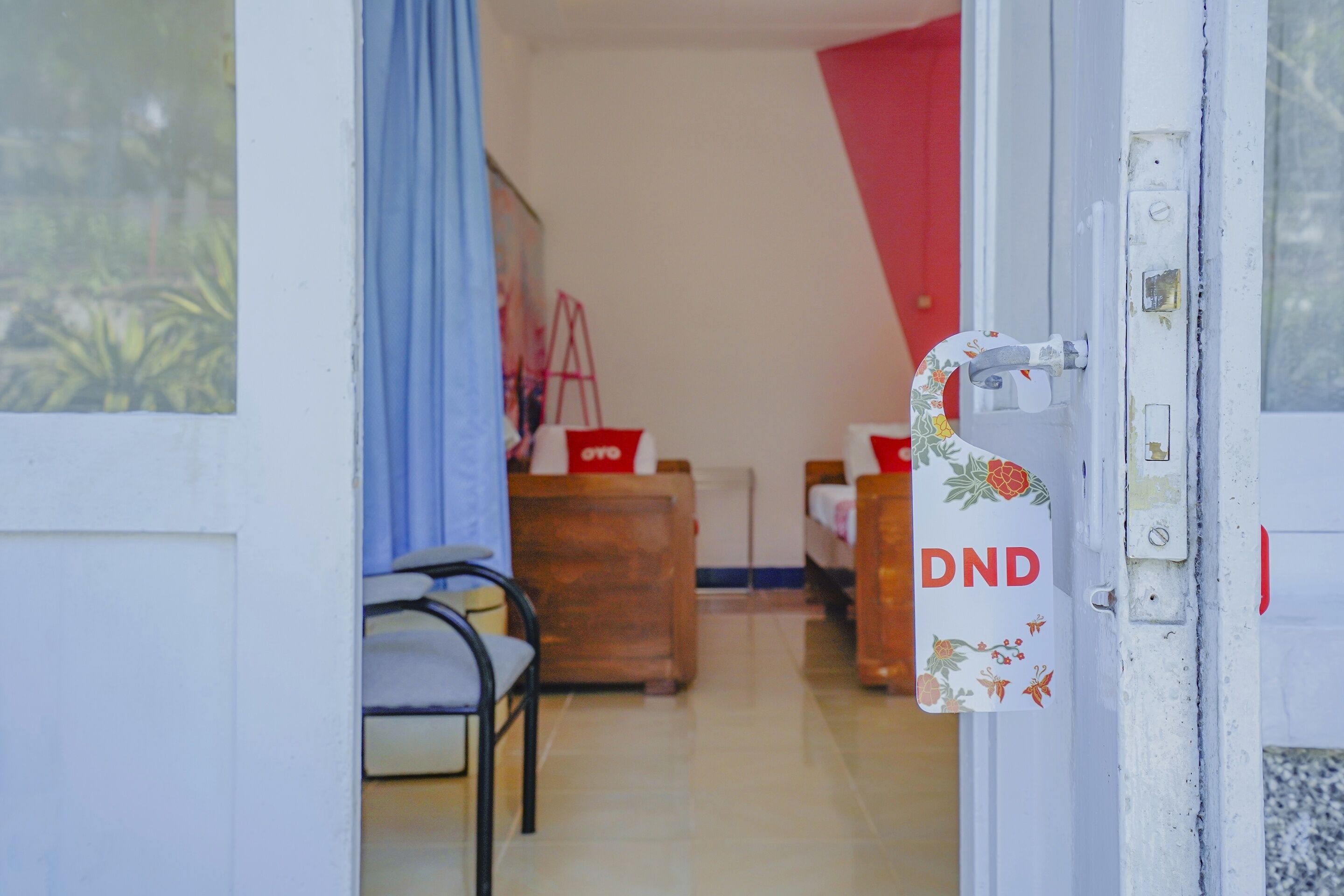 Habitación de hotel con cama, cómoda de madera y una silla. Se observa una puerta con el letrero que dice "DND".