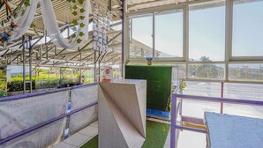 A greenhouse with a transparent roof, allowing natural light to illuminate the interior. Inside, there are various plants and a display of packaged goods on shelves. - OYO 90352 Villa Agape 2 (Cipanas)