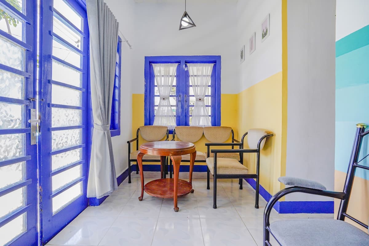 Quarto com porta azul, mesa de madeira redonda, dois sofás bege e uma cadeira preta.