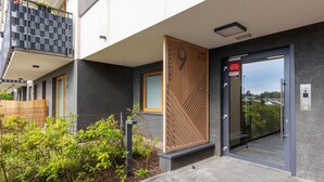 A modern building with a grey facade, a wooden decorative panel, and a glass door with a sign.
