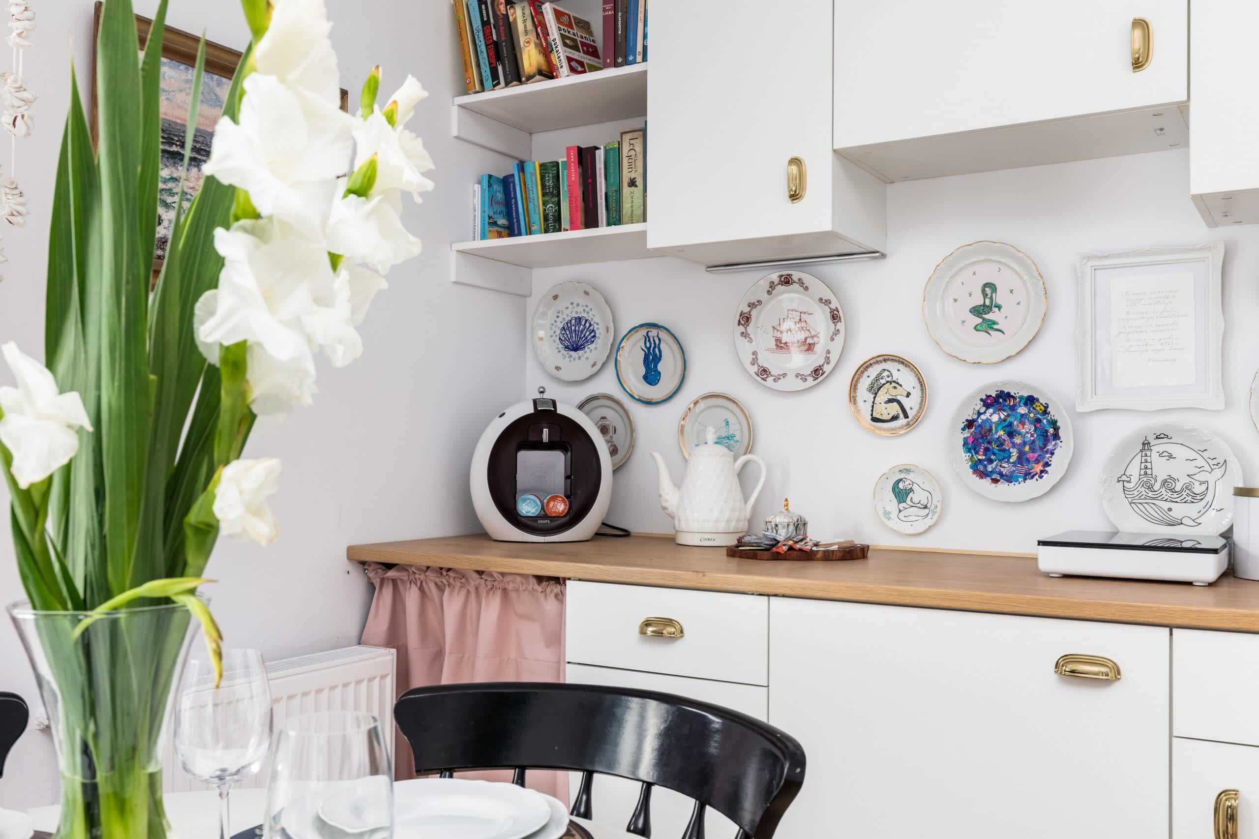 Une cuisine avec des meubles blancs, un plan de travail en bois et diverses assiettes décoratives.