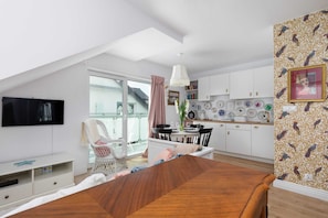 A modern bedroom with a sloped ceiling, a TV, a wooden bed, a balcony with a chair, and a dining area with a table and chairs.