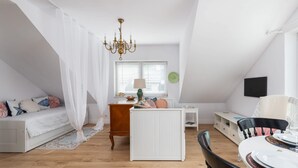 Una habitación con una cama, un radiador blanco, una mesa con sillas, una araña y una ventana con persianas.